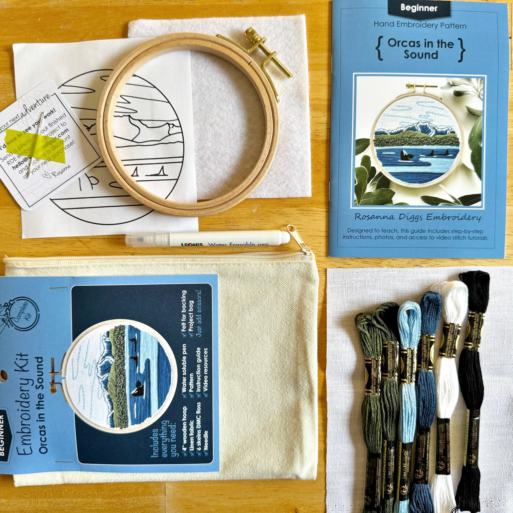 Embroidery kit with hoop, fabric, thread, and pattern book on a wooden surface.