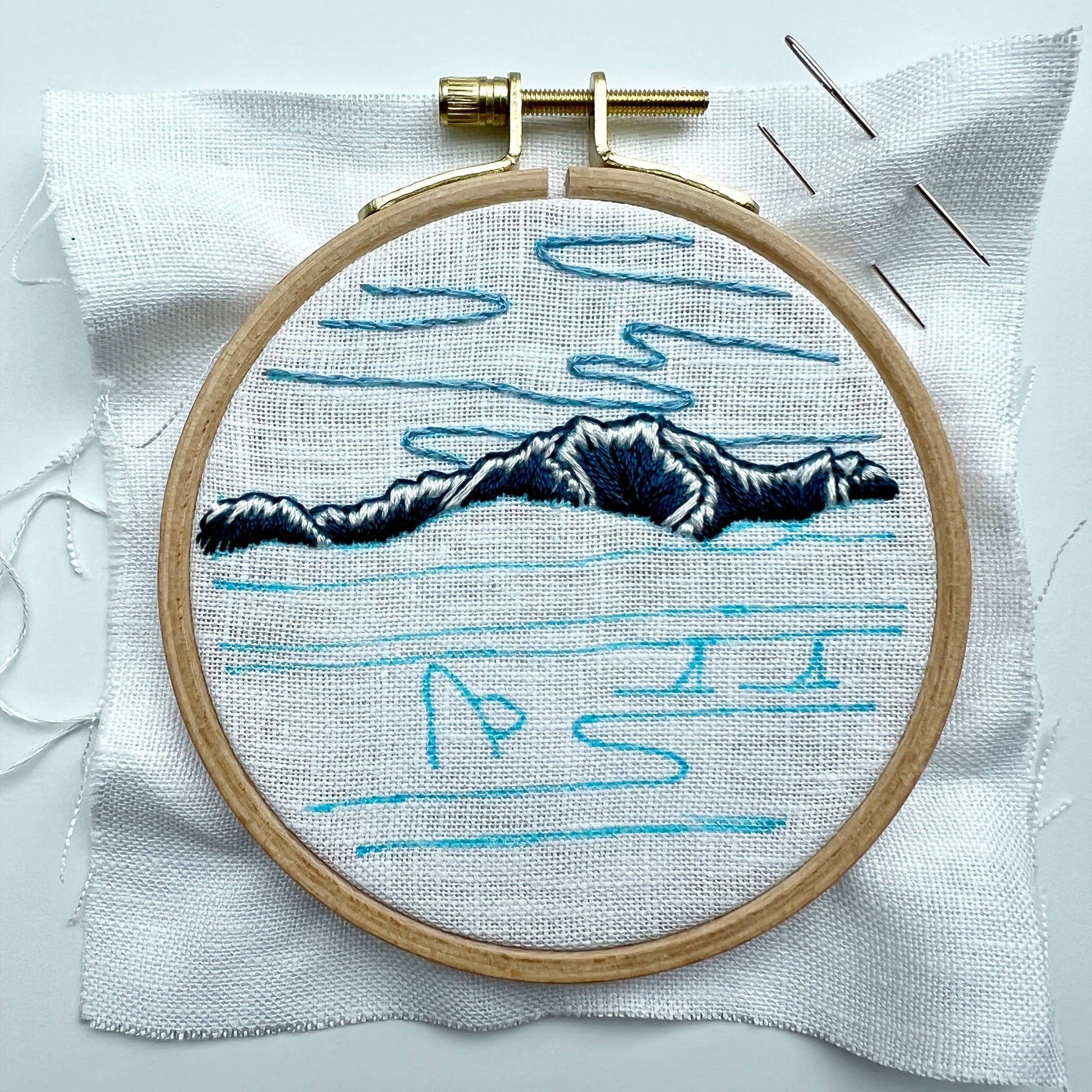 Embroidery hoop with a mountain design and traced pattern on white fabric