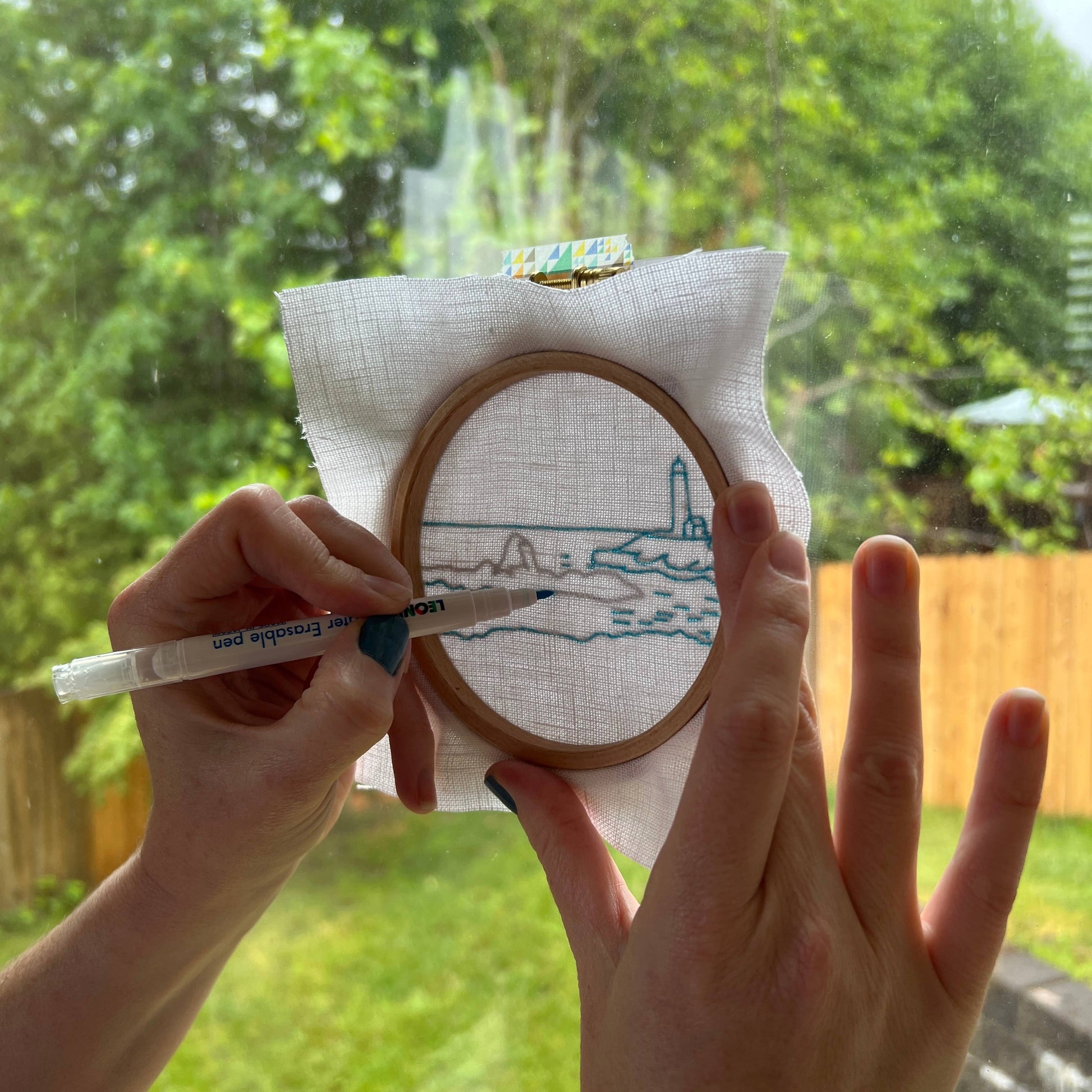 Person holding an embroidery hoop and tracing the design pattern outdoors.