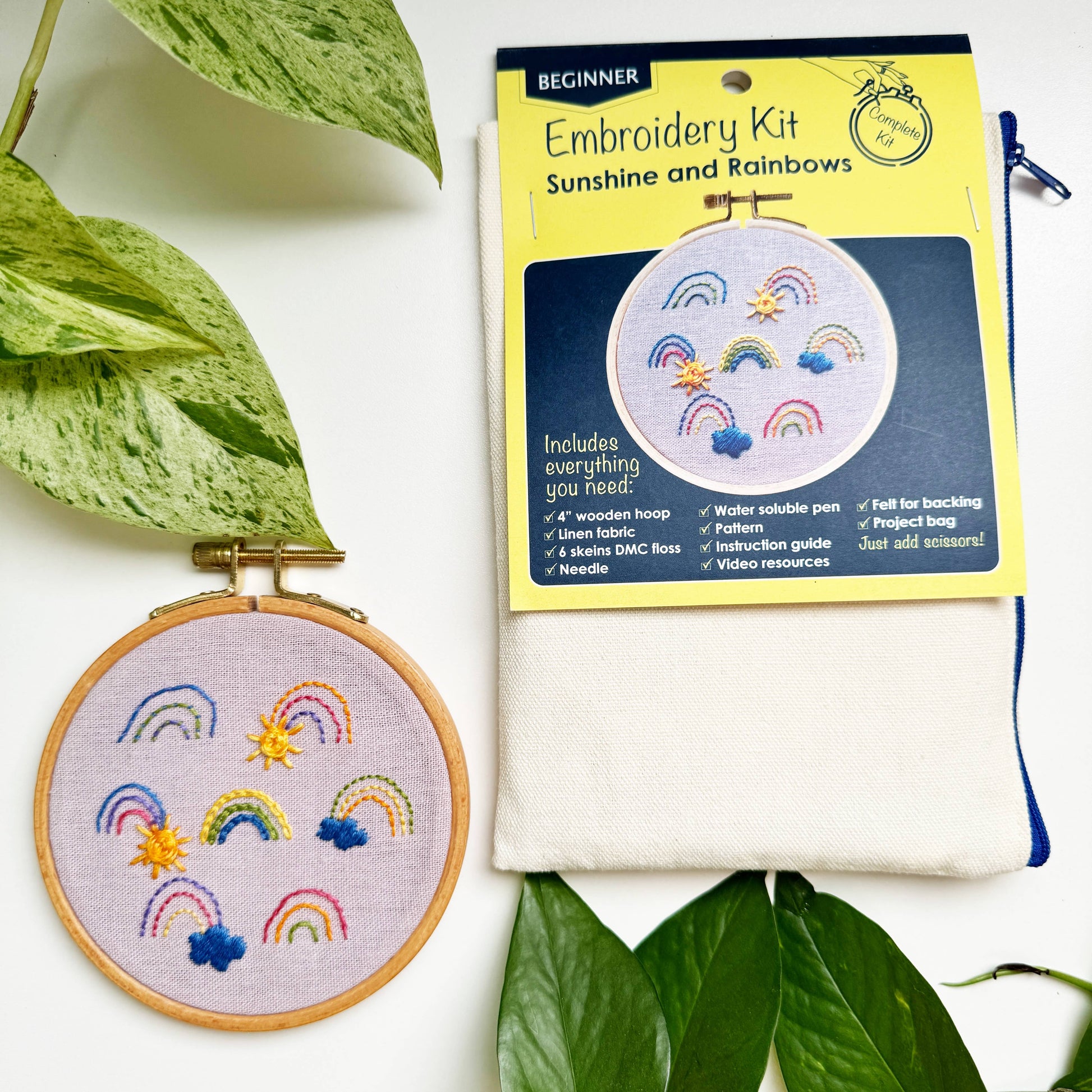 Embroidery kit with completed embroidery piece and packaging on a white background with green leaves.