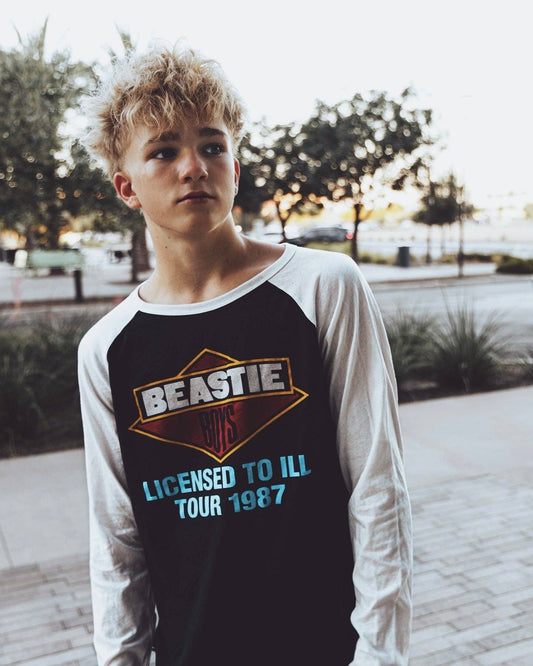 A kid wearing a Beastie Boys licensed to ill tour shirt outdoors.