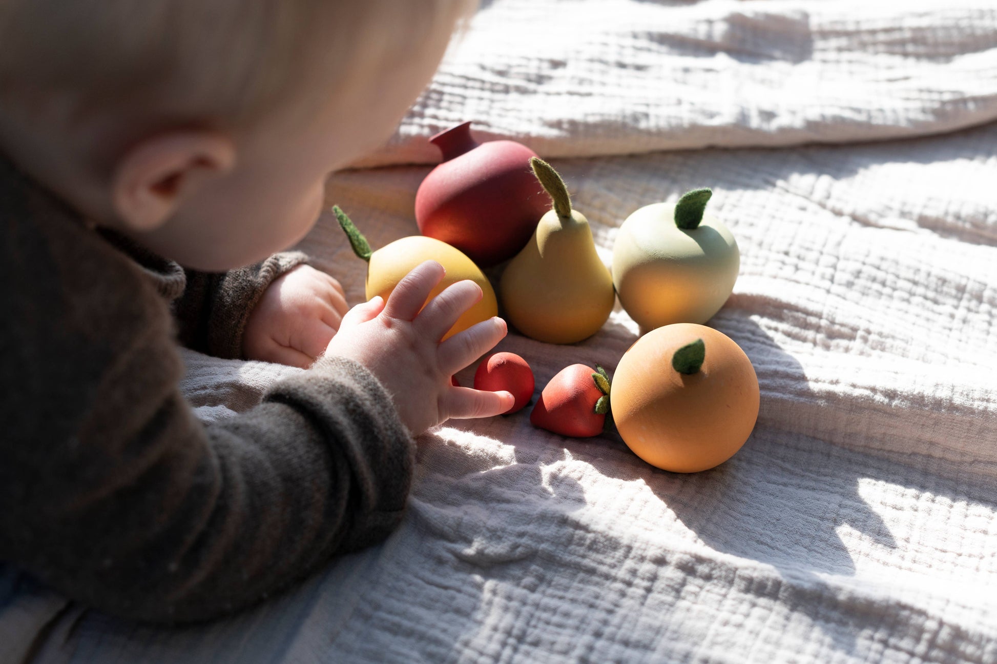 a baby laying on a bed playing with wooden toy fruits