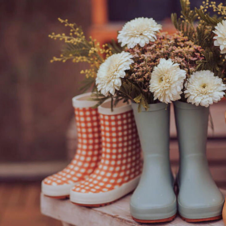 Two pairs of rain boots with flowers inside on a wooden surface.