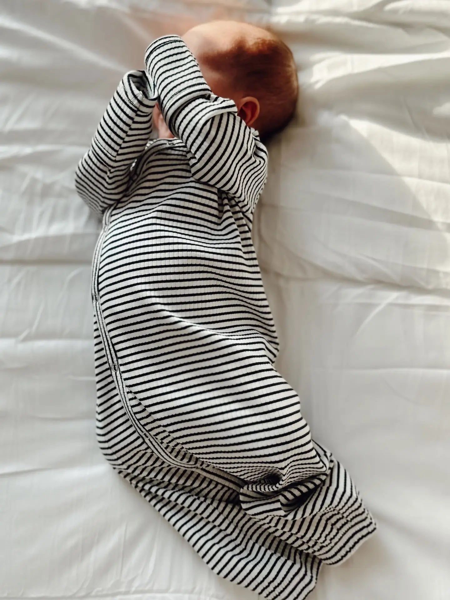 Baby swaddled in a black and white striped gown on a white bed.