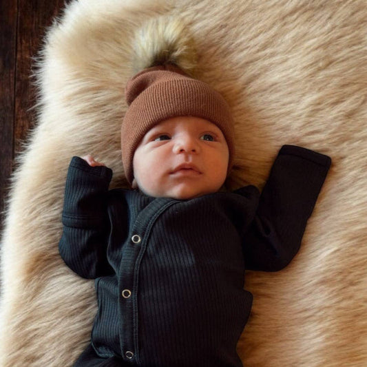 Baby in a black gown and brown hat lying on a fur rug