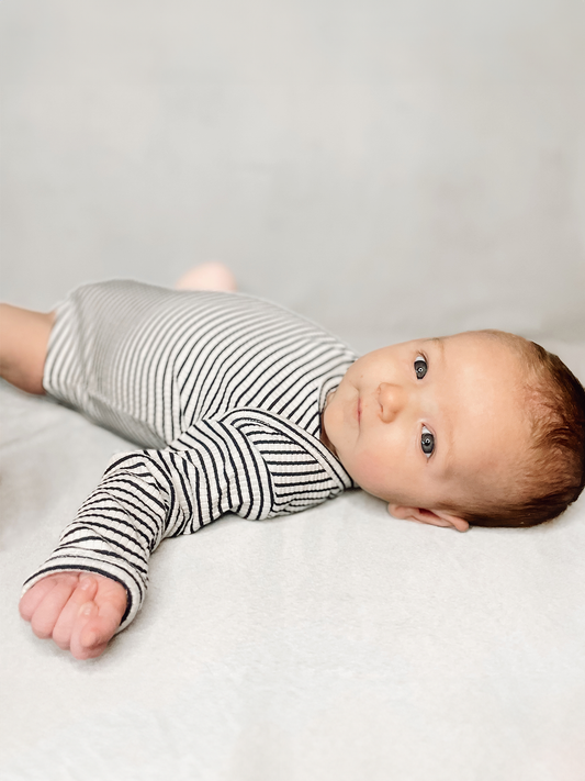 Baby wearing a black and white striped onesie lying on a light gray blanket