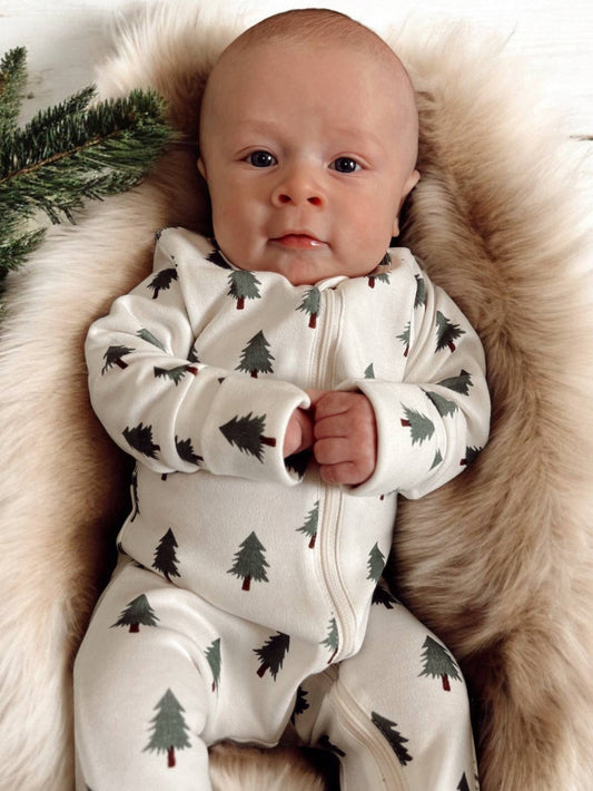 Baby wearing a white zip romper with tree patterns, lying on a fluffy beige blanket