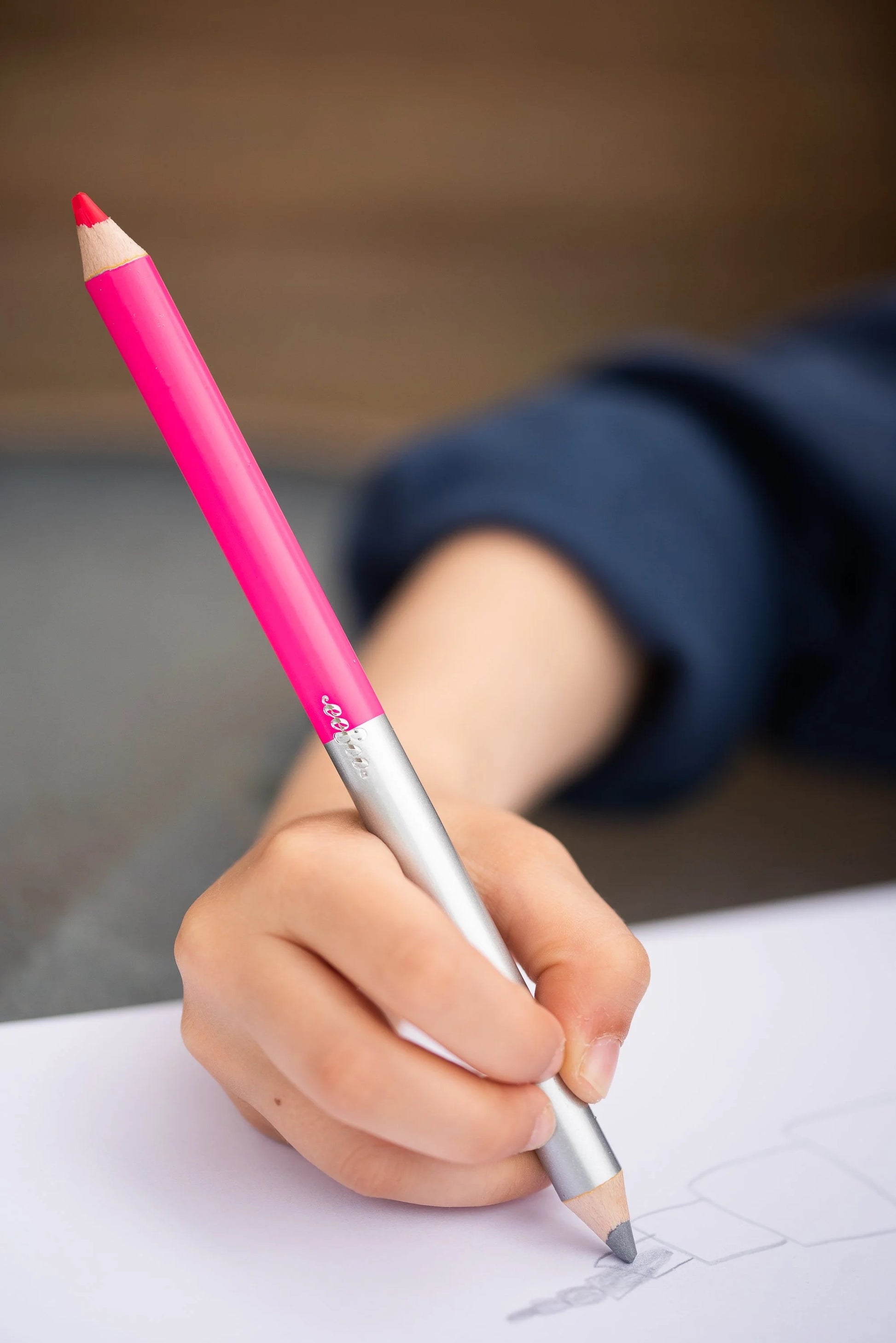 child wearing a blue sweater drawing with the silver side of a metallic double-sided jumbo pencil