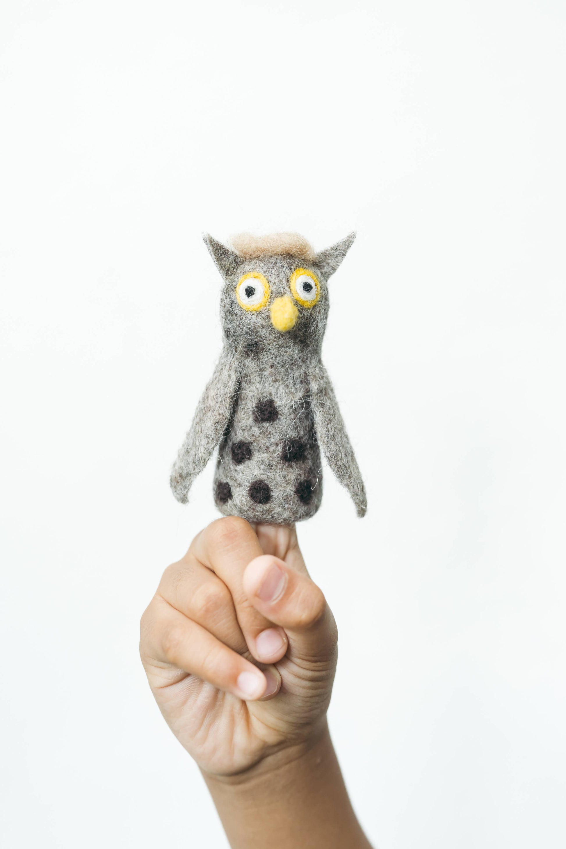 Hand holding a small owl-shaped finger puppet against a white background