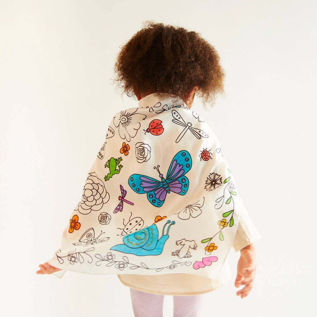 A child standing with their back to the camera wearing a coloring playsilk as a cape