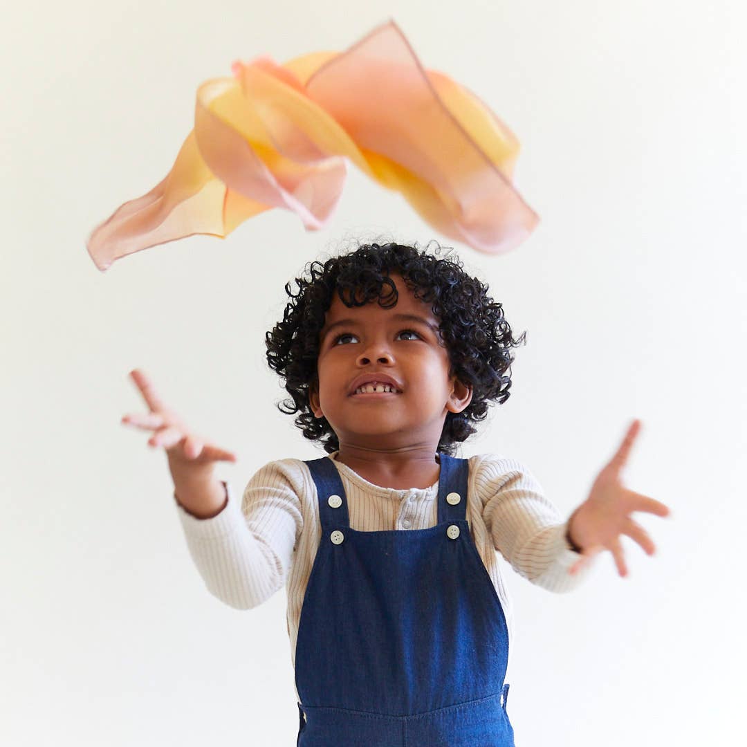 A child throwing a desert mini playsilk in the air