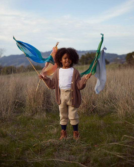 A child standing in a field holding four wooden sticks with playsilks tied to the ends