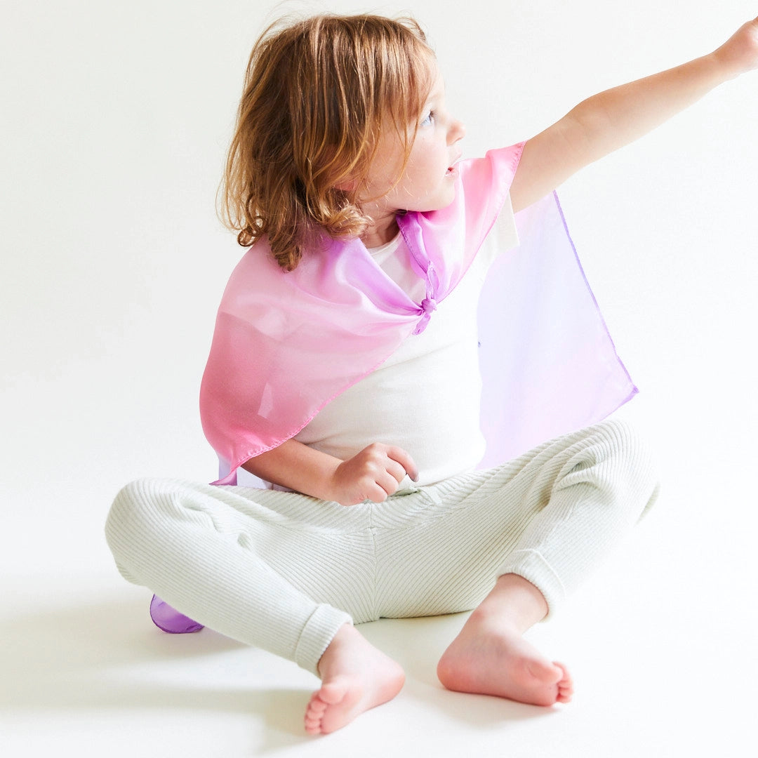 child sitting on the floor wearing blossom mini playsilk as a cape