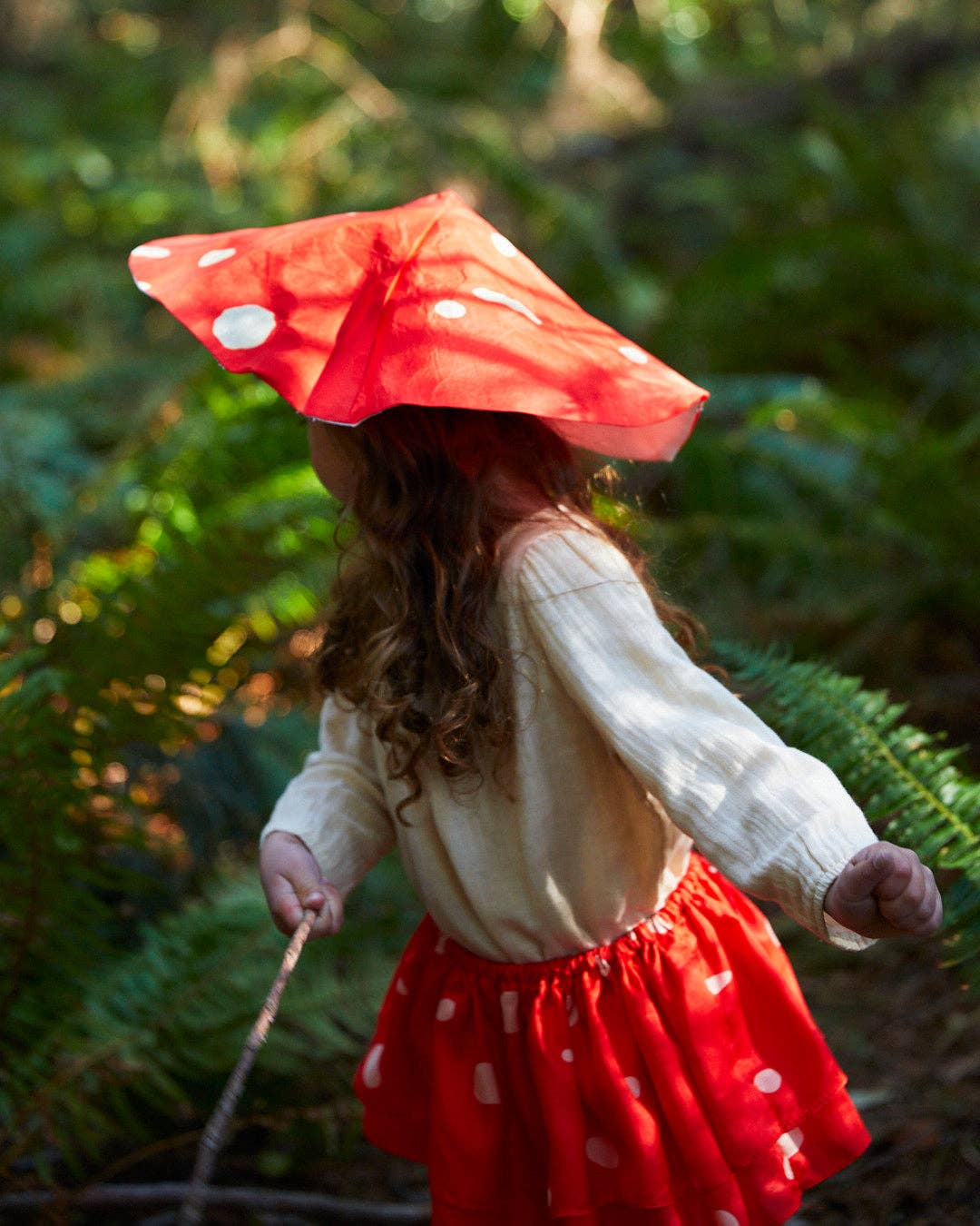 A child standing in the woods wearing a silk mushroom costume with hat and tutu