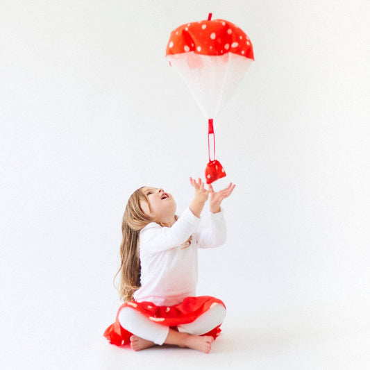 Child holding a red mushroom parachute toy against a white background