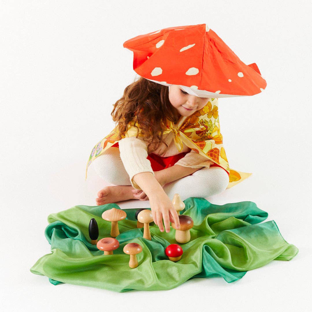 child wearing a silk mushroom hat playing with wooden mushroom set