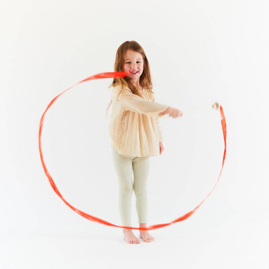 Young child playing with a red mushroom streamer wand on a white background