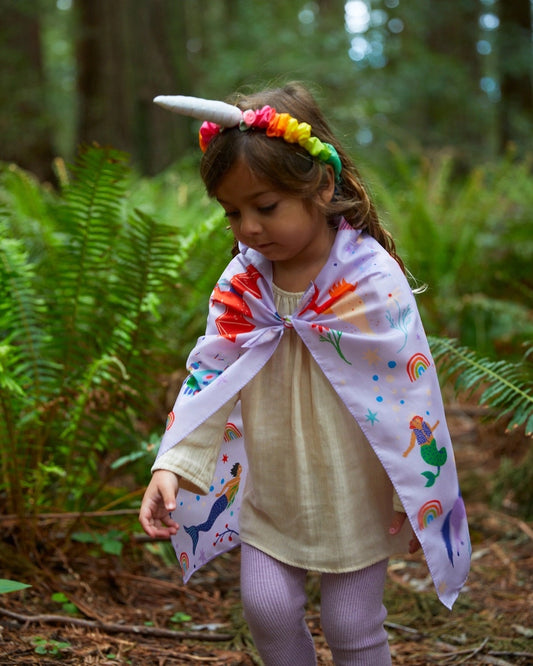 Child wearing a playsilk cape and a unicorn silk headband in the woods