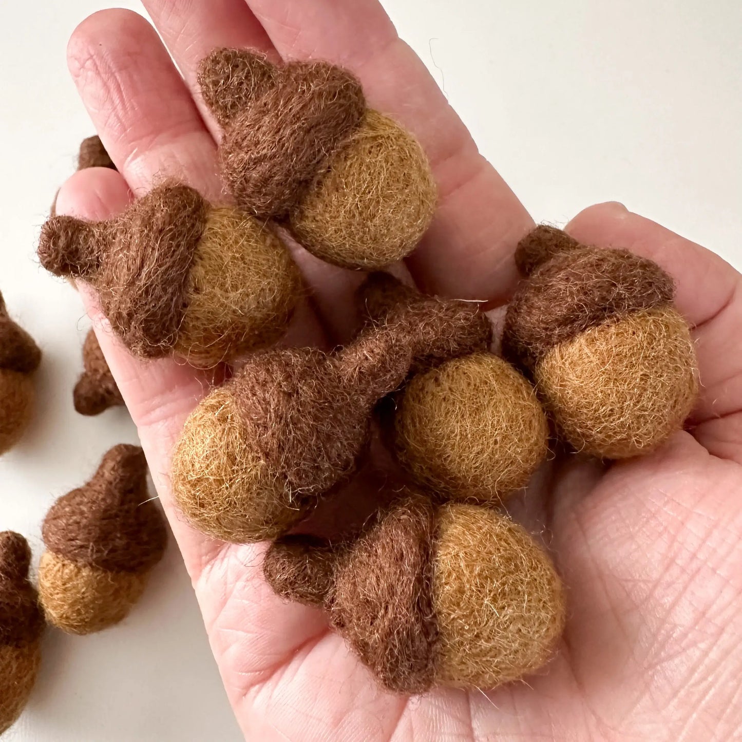 hand holding six brown felt acorns