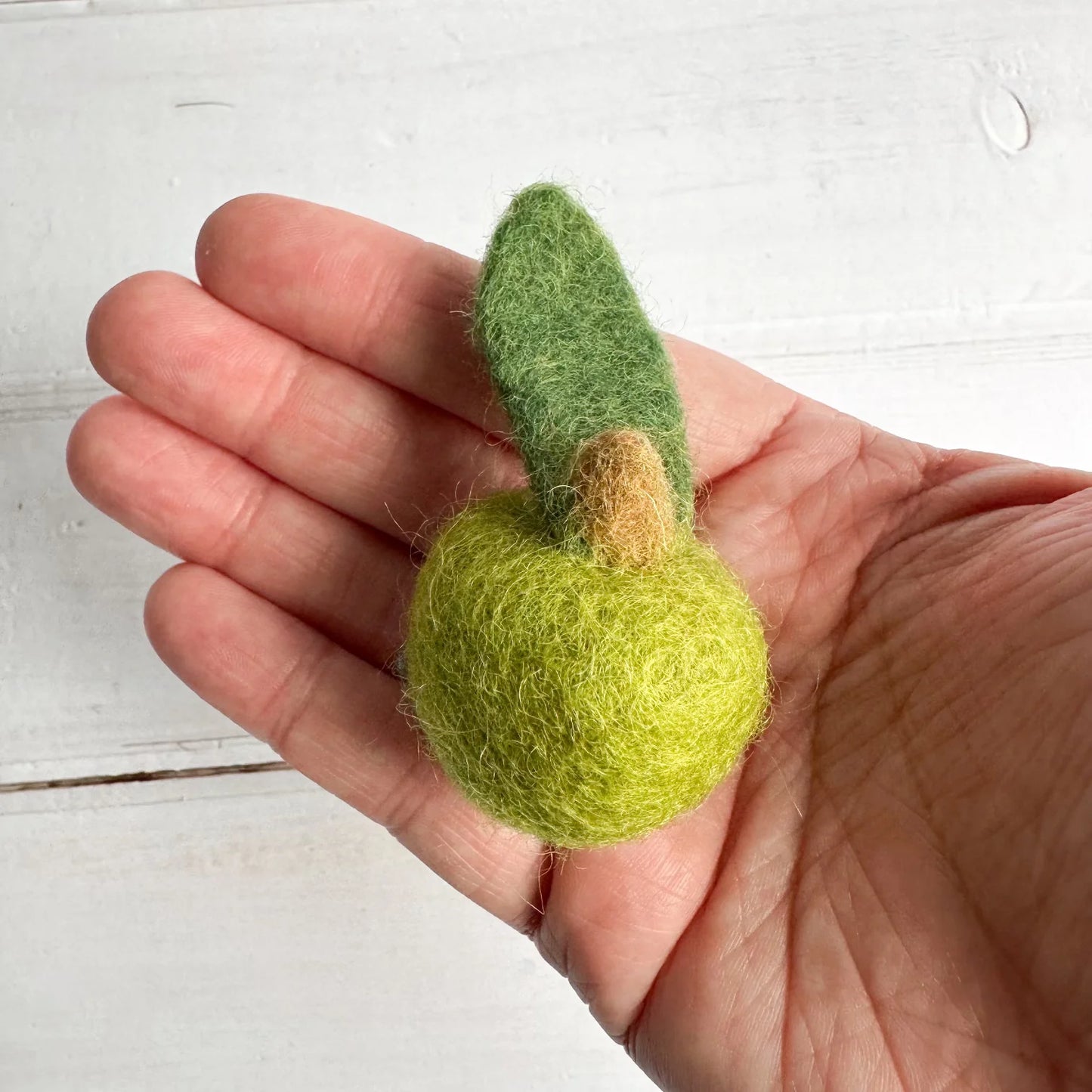 a hand holding a mini felt green apple