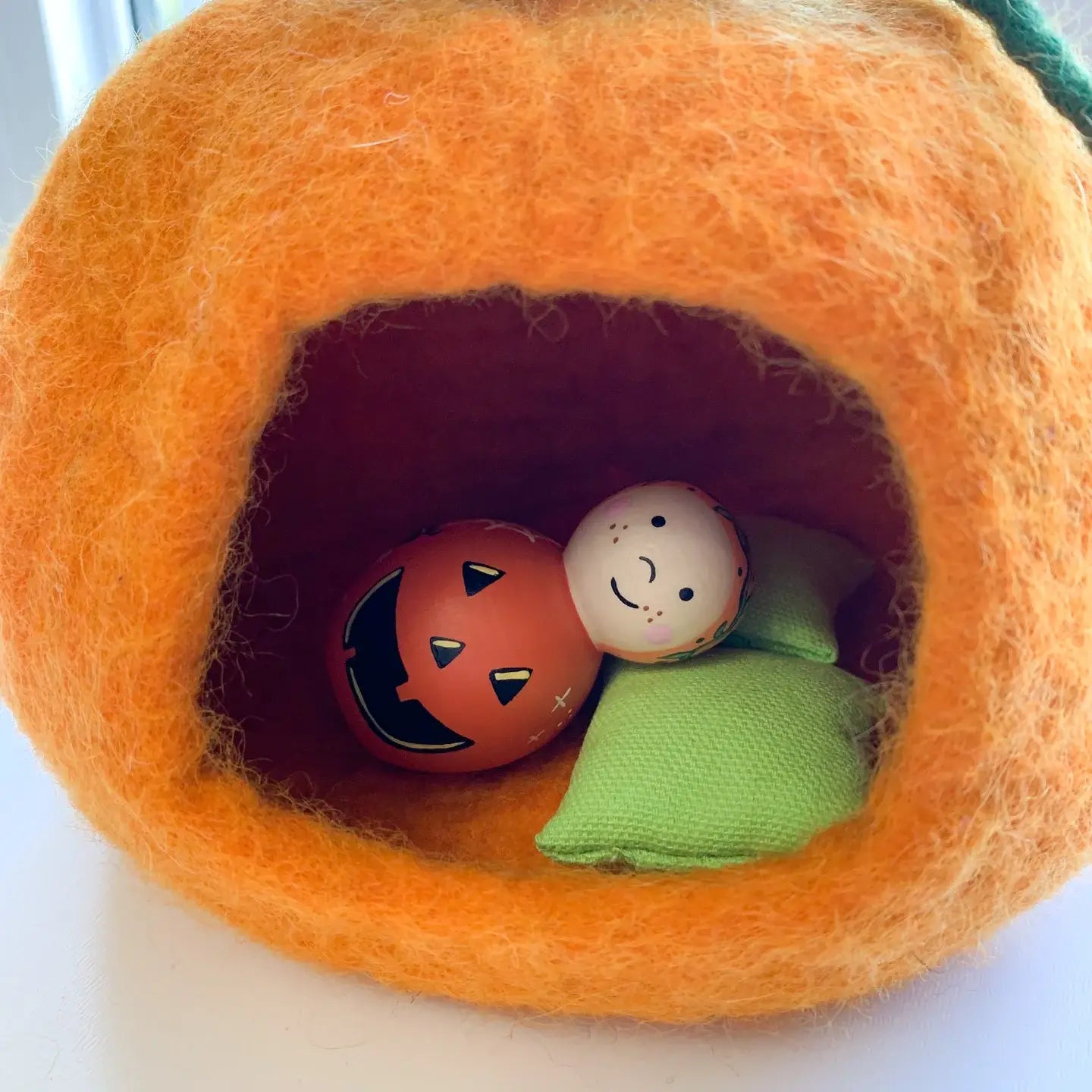 wooden doll laid down in a felt pumpkin cottage