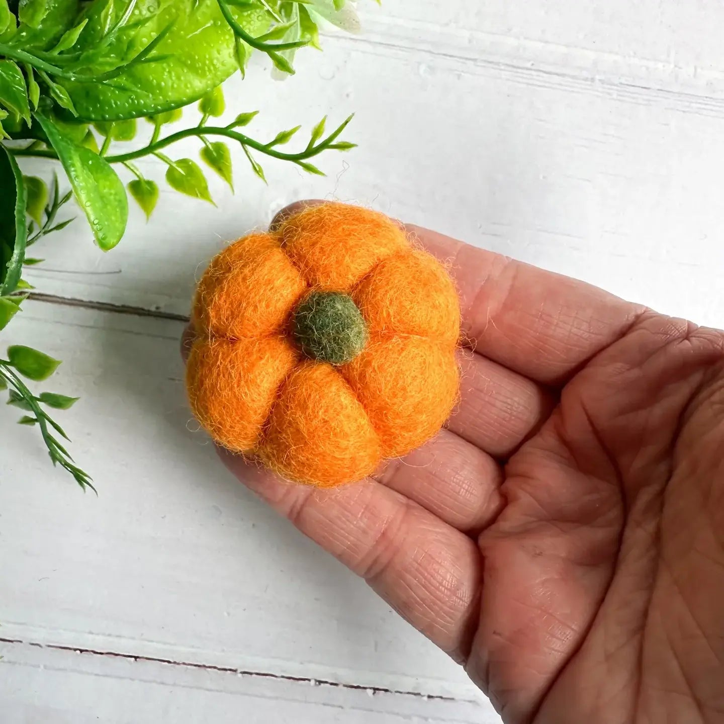 A hand holding an orange mini felt pumpkin