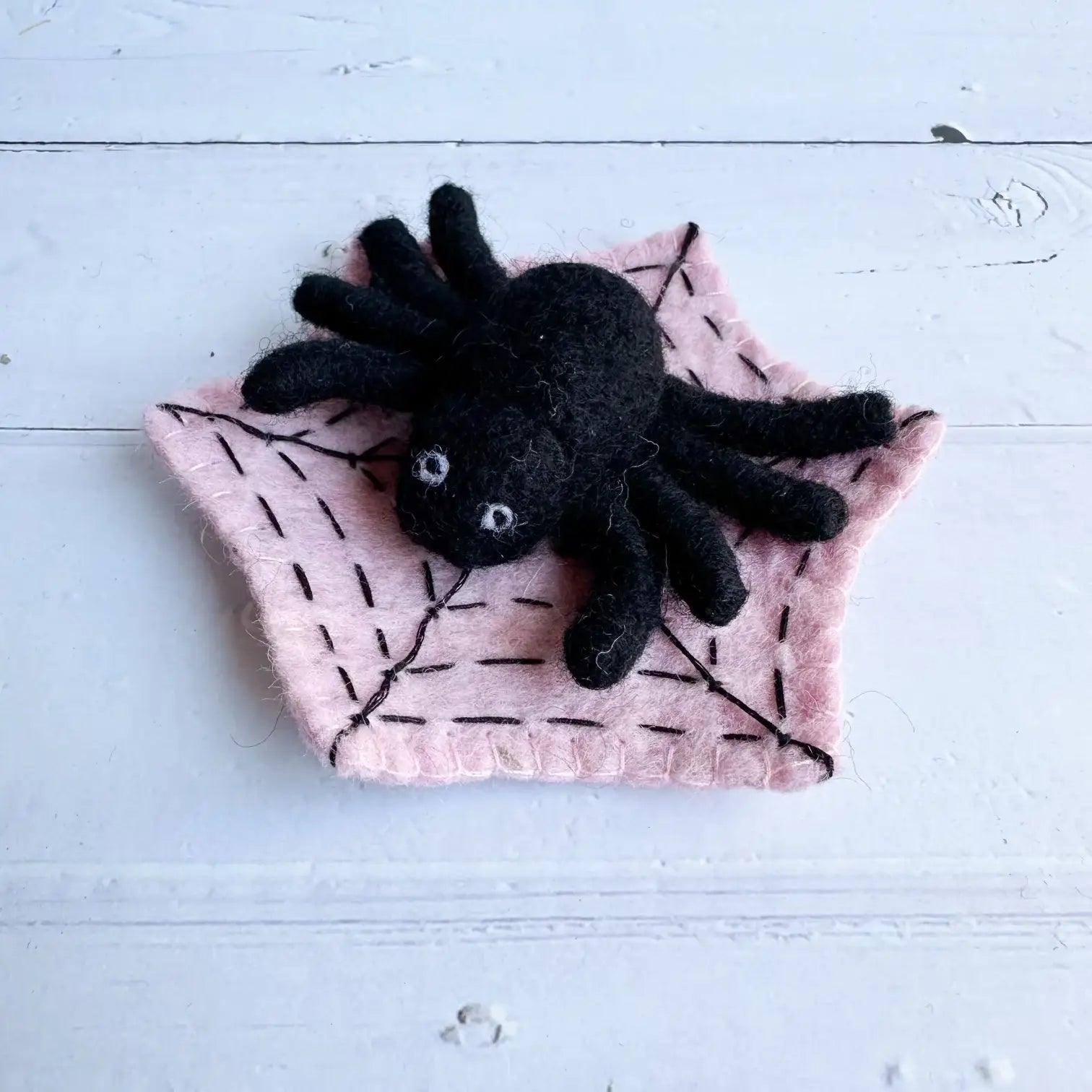 Black felt spider on a pink felt spider web