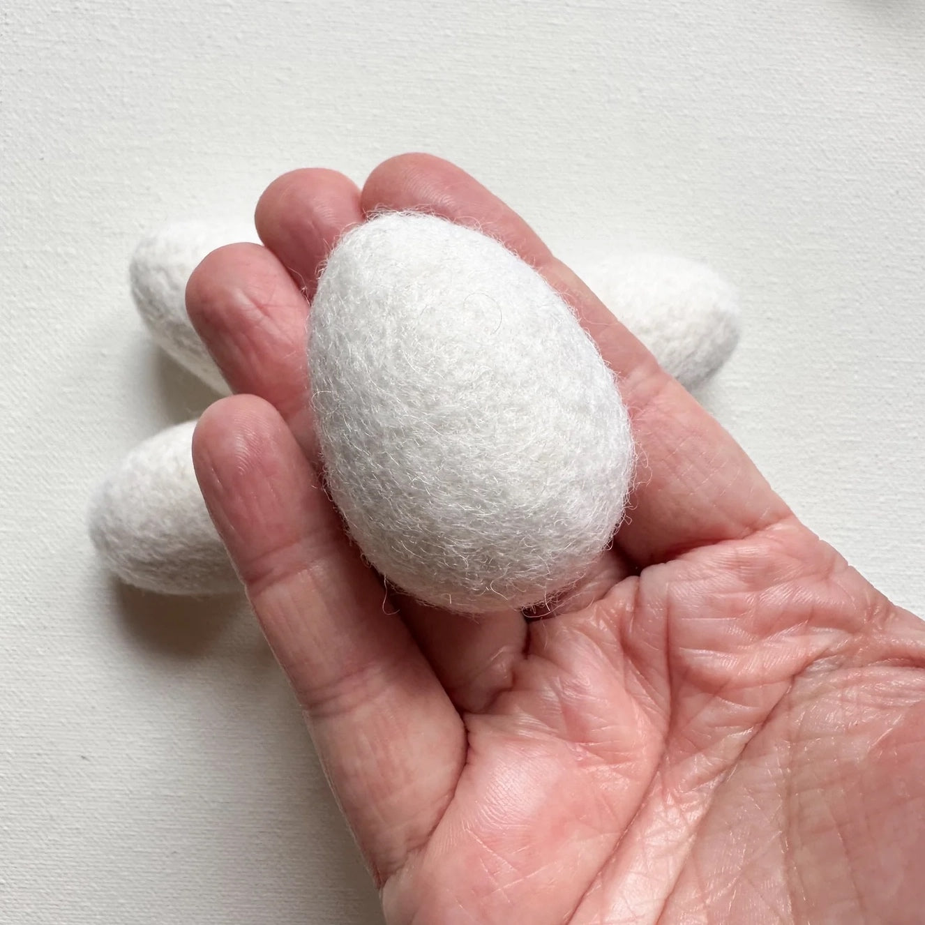 hand holding one white felt egg