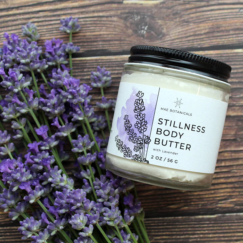 Stillness body butter 2oz jar on a wooden table next to a bunch of lavender