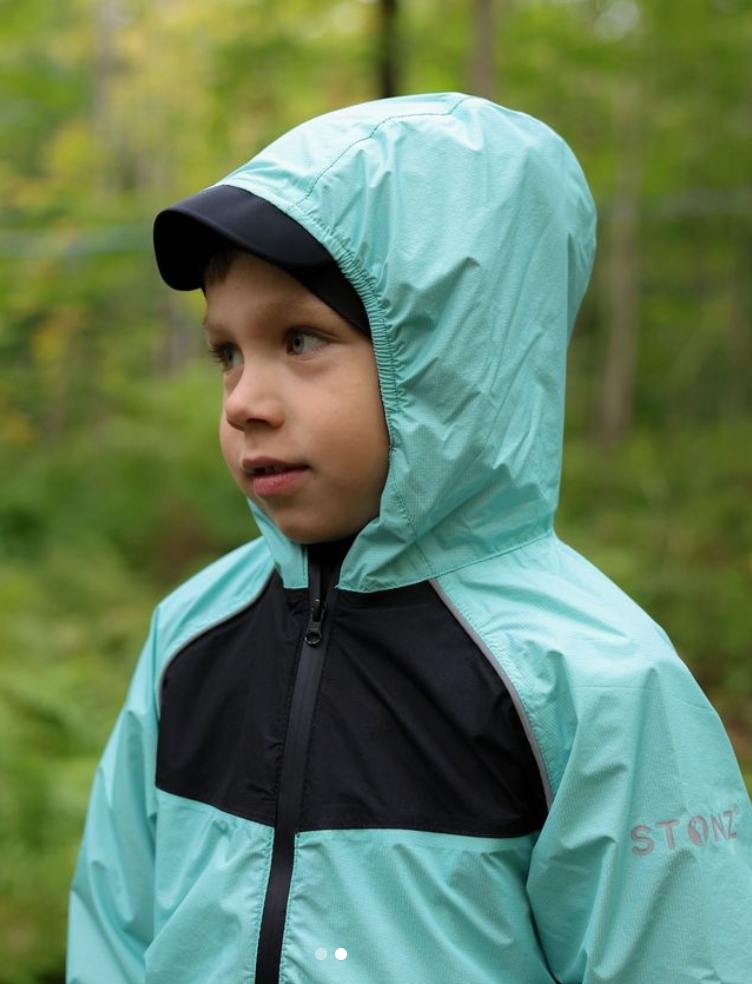 Child standing in the woods wearing a teal rain suit