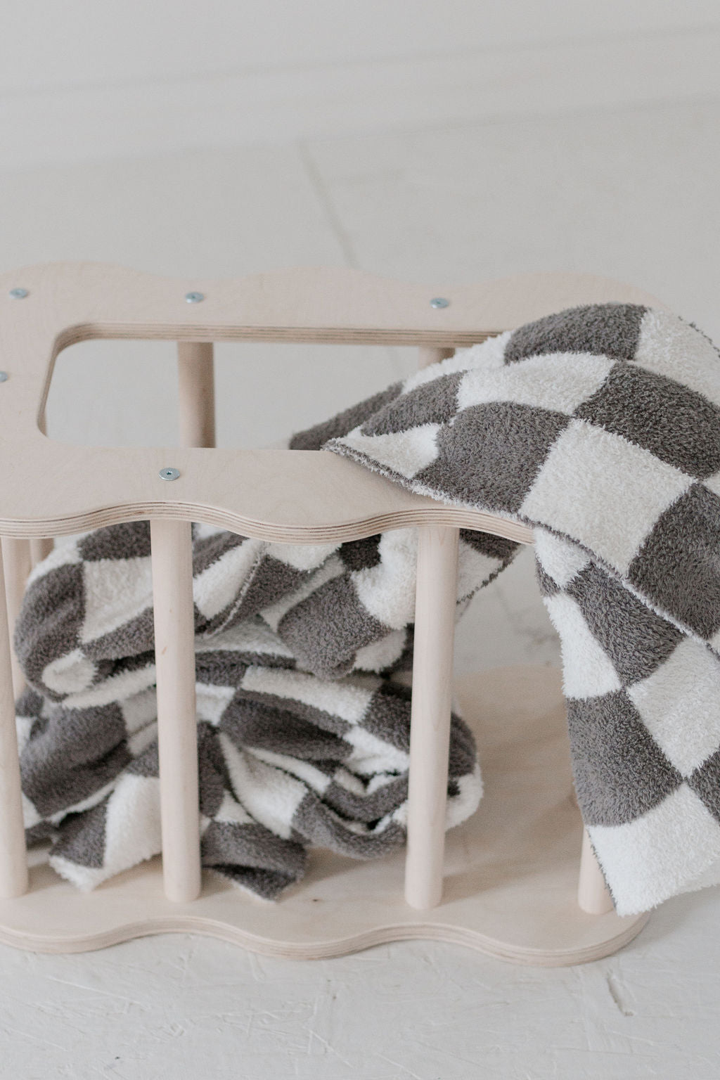 Checkered blanket draped over a wooden crib on a light background