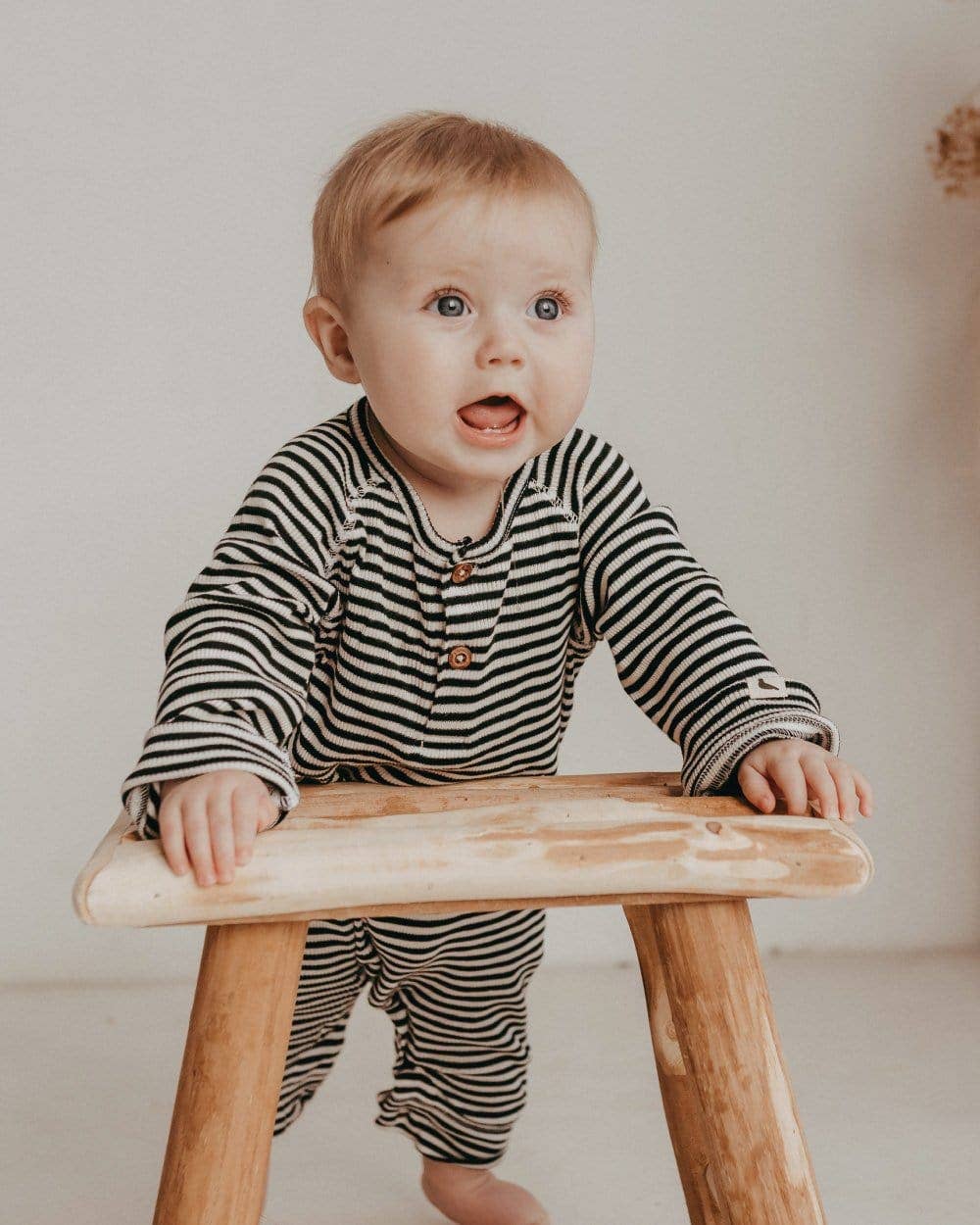 baby holding themselves up on a wooden stool wearing striped long-sleeve romper