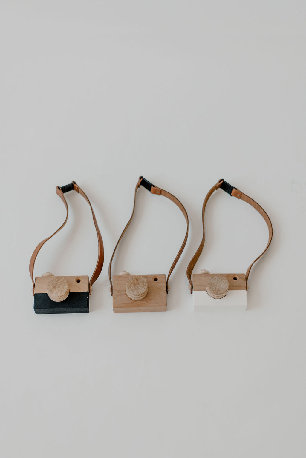 Three wooden camera-shaped objects with leather straps on a light gray background