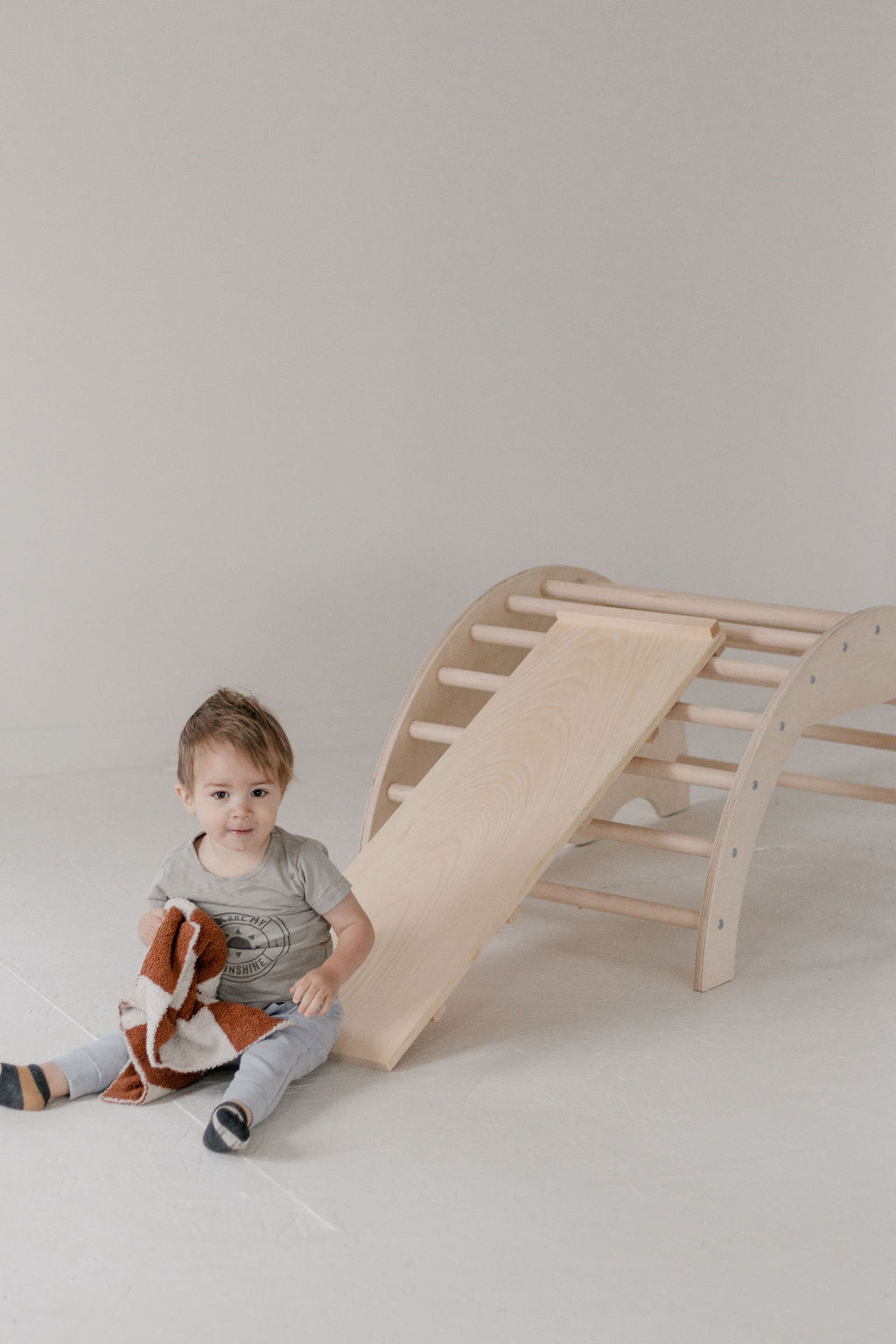 Child sitting next to a wooden climbing toy on a plain background