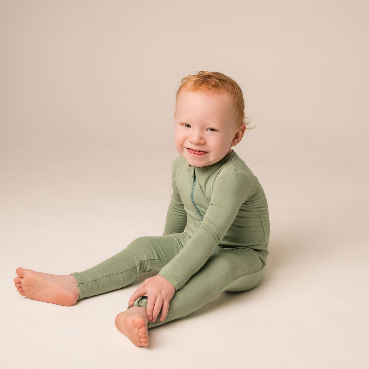 Child wearing a green outfit sitting on a beige background