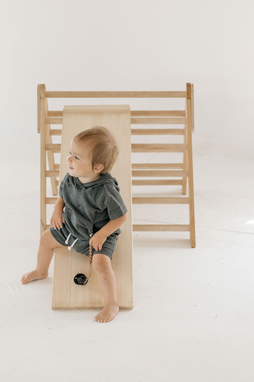 Child sitting on a wooden climbing toy against a white background