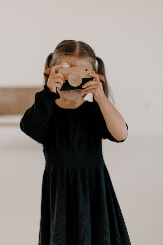 Child in a black dress holding a camera against a plain background