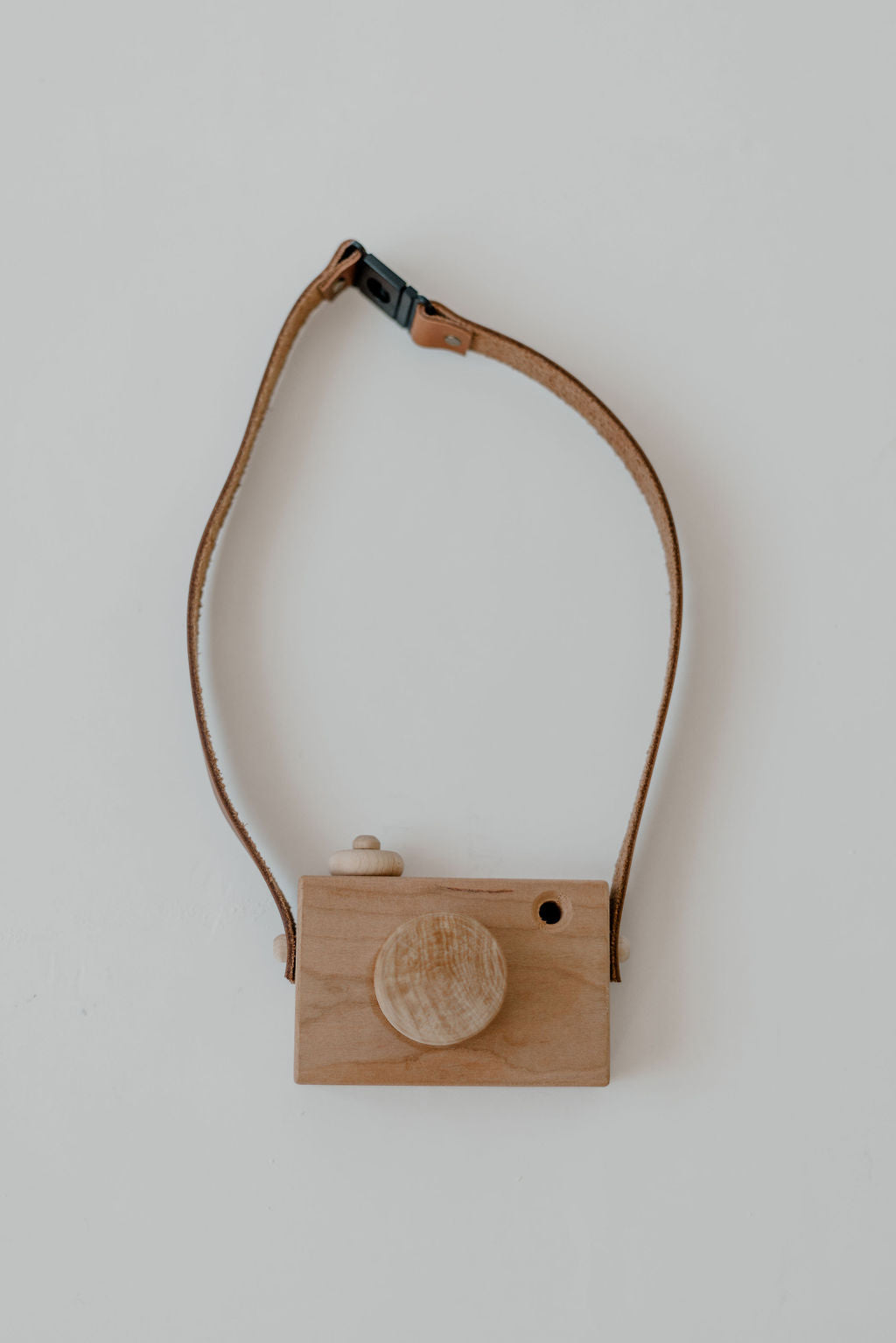 Wooden camera-shaped object with a leather strap on a light background