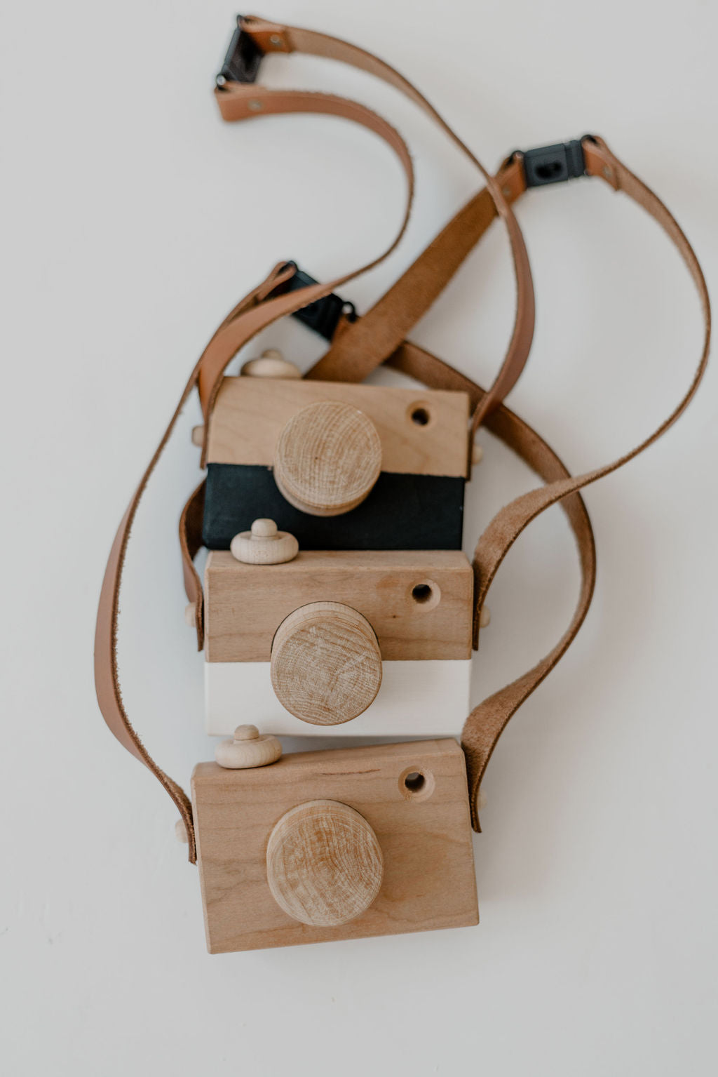 Stack of wooden toy cameras with a leather strap on a white background