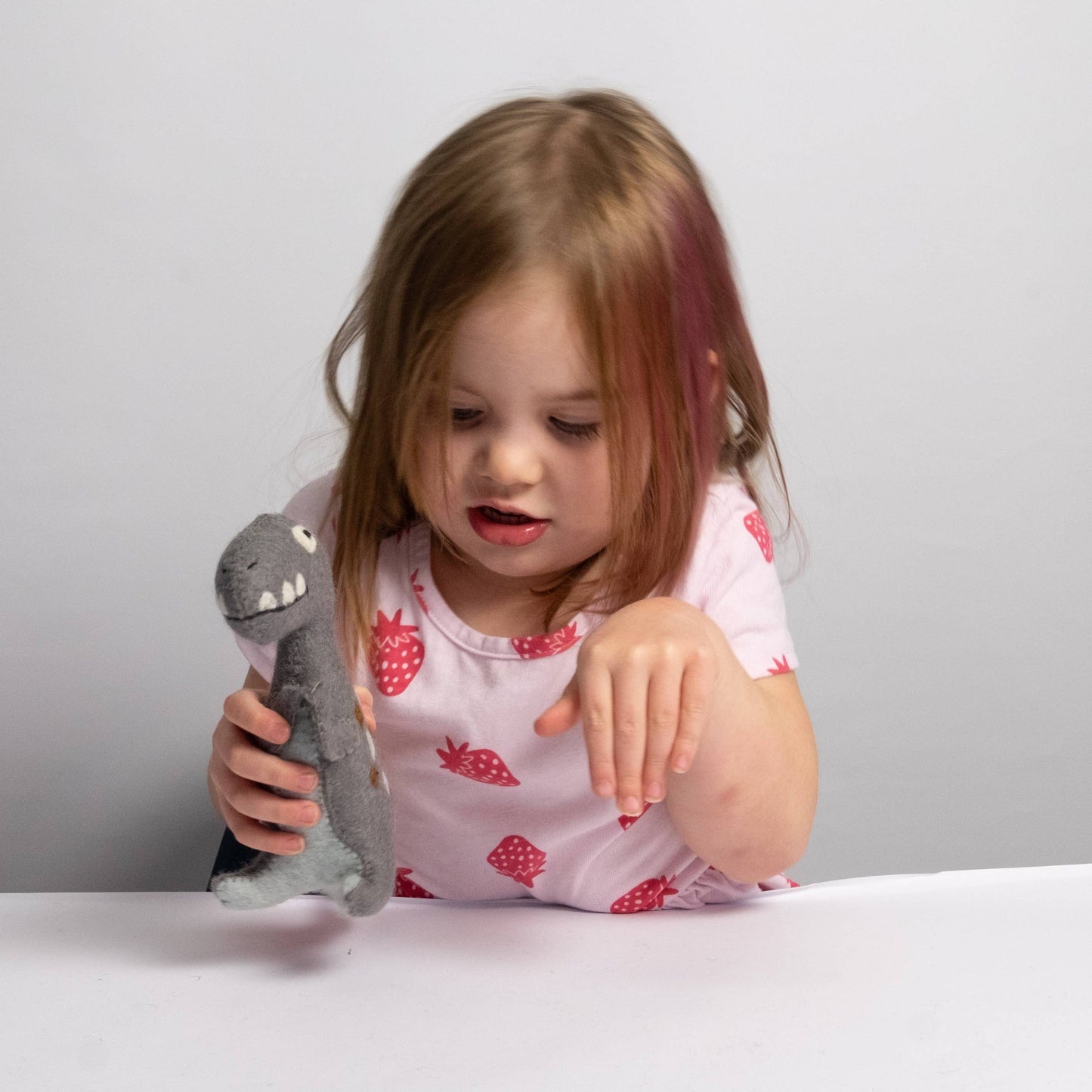 Child holding a felt dinosaur plush toy with a plain background