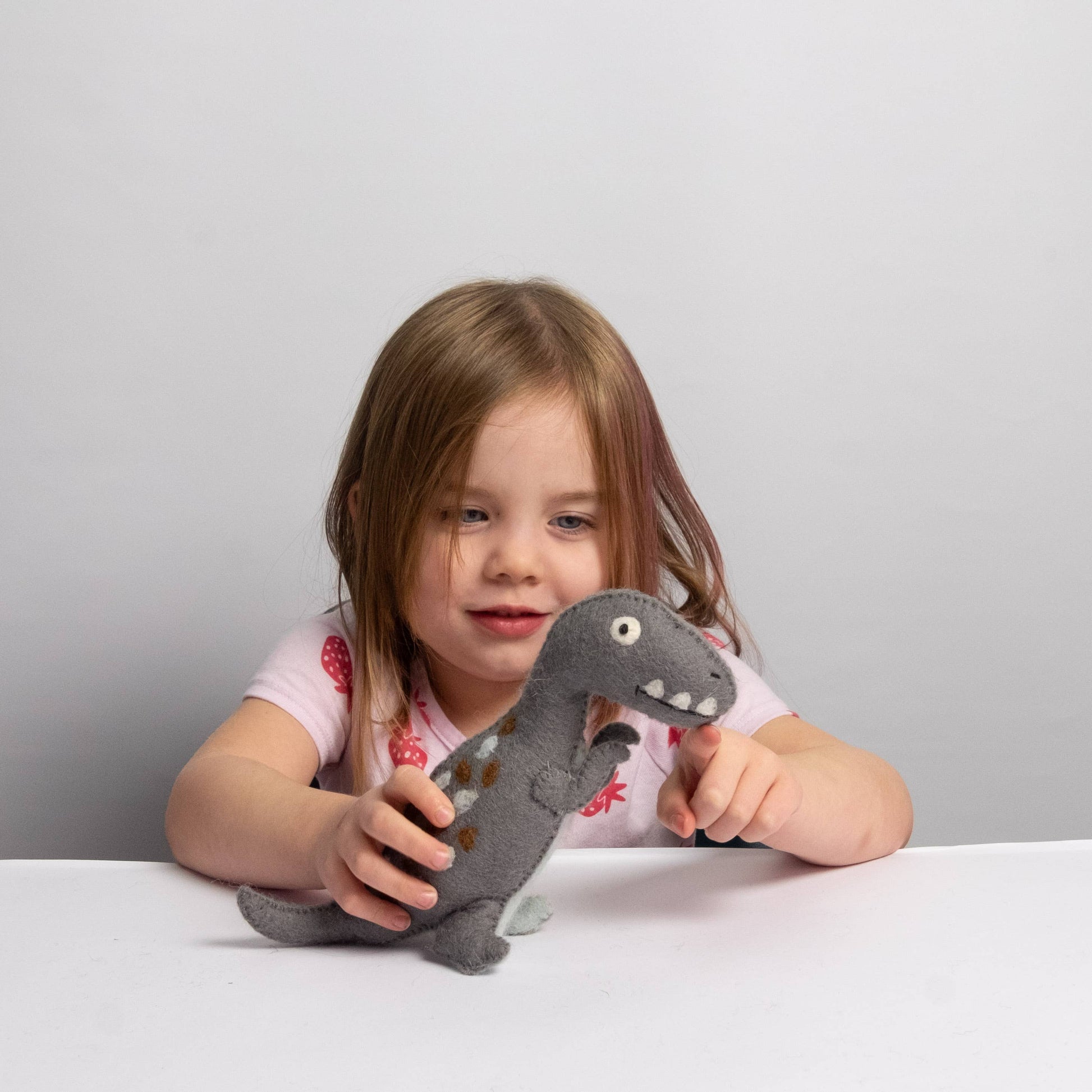 Child holding a plush dinosaur toy against a plain background