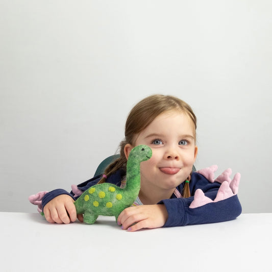 Young child holding a green dinosaur toy against a plain background
