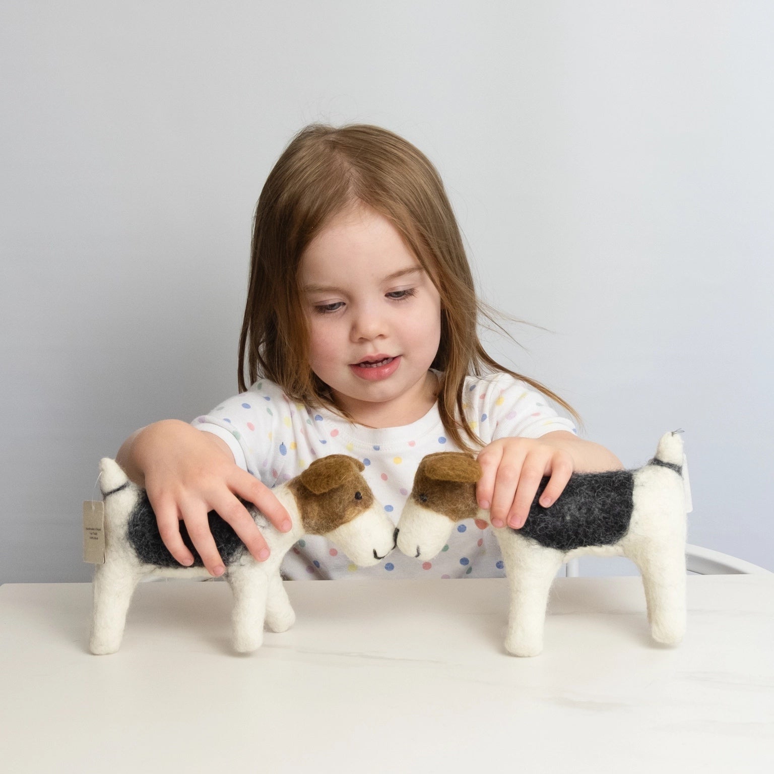 child playing with two wool felt dogs on a white table