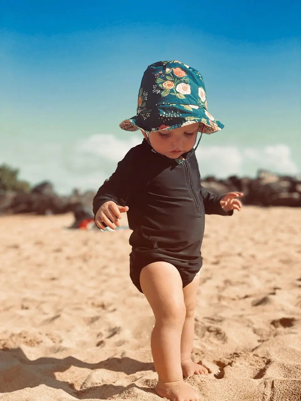 Baby walking on the beach wearing Organic Reversible Aullwood Bucket Hat