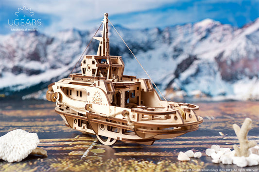 Wooden model ship on a wooden surface with mountains in the background