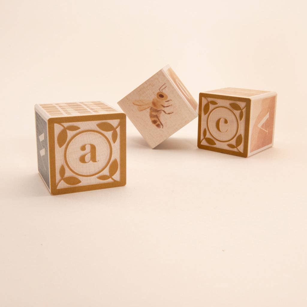 Three wooden blocks with letter 'a', bee, and letter 'c' on a beige background