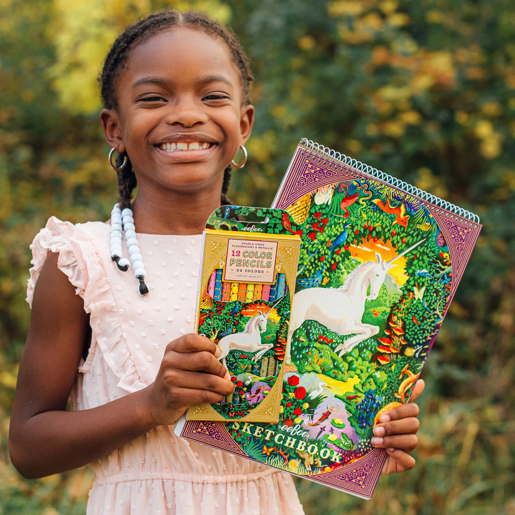 child standing outside holding a unicorn notebook and pencil set
