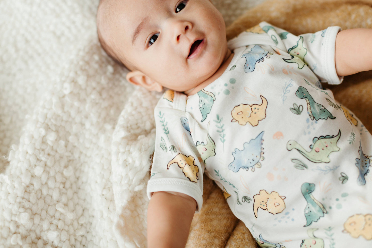 baby laying on a fuzzy blanket wearing a dinosaur print short sleeve onesie
