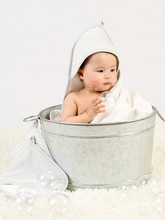 baby sitting in a metal tub wrapped in a grey striped hooded towel