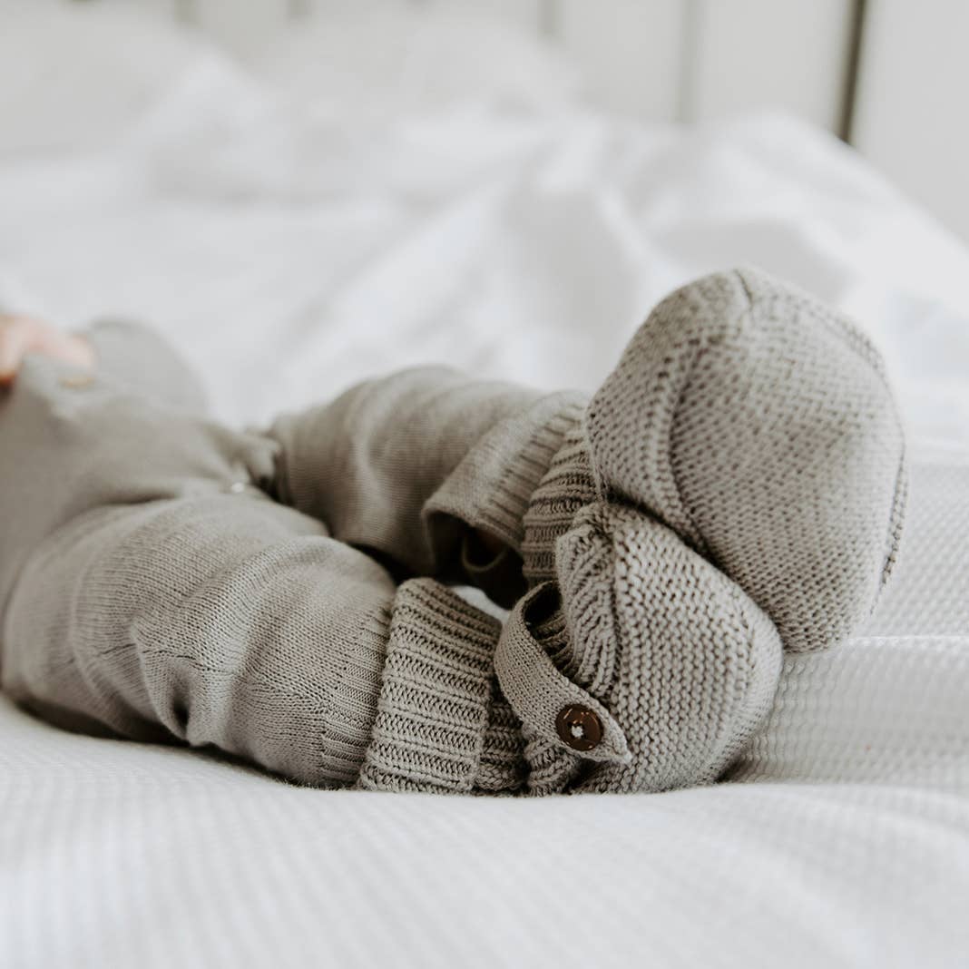 Close-up of baby's feet wearing gray knit booties on a white bed